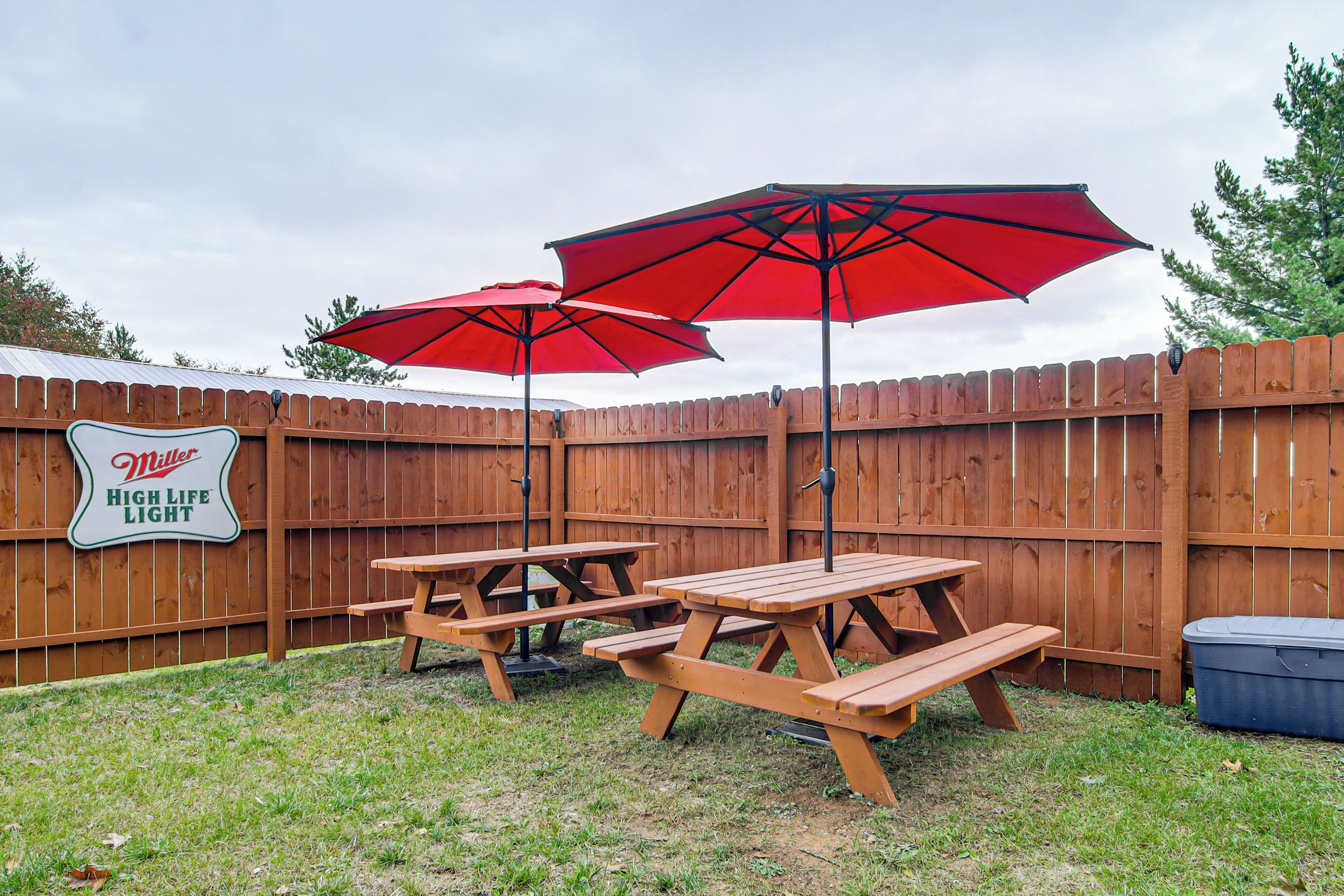 A backyard with a wooden fence, picnic tables, and red umbrellas.