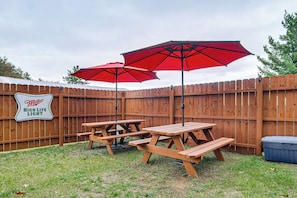 A backyard with a wooden fence, picnic tables, and red umbrellas.