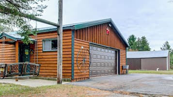 A wooden cabin with a garage, a swing set, and a metal wheel.