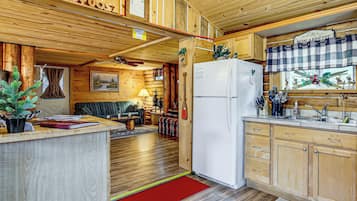 A cabin interior with a wooden interior, a dining area, a kitchen with a refrigerator, and a fireplace.