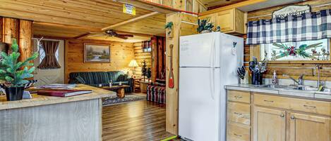 Ein Blockhaus-Interieur mit Holzausstattung, einem Essbereich, einer Küche mit Kühlschrank und einem Kamin.