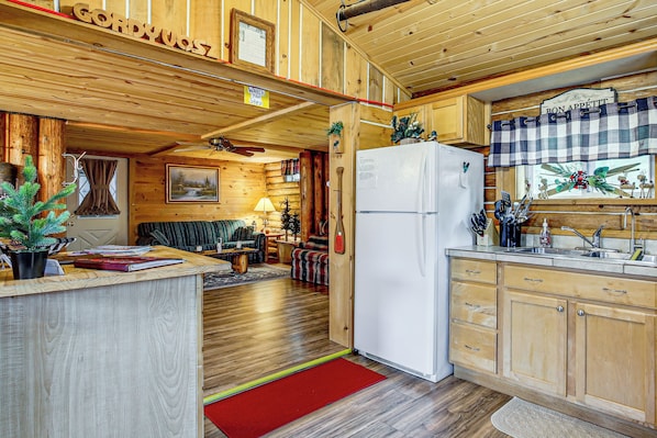 A cabin interior with a wooden interior, a dining area, a kitchen with a refrigerator, and a fireplace.