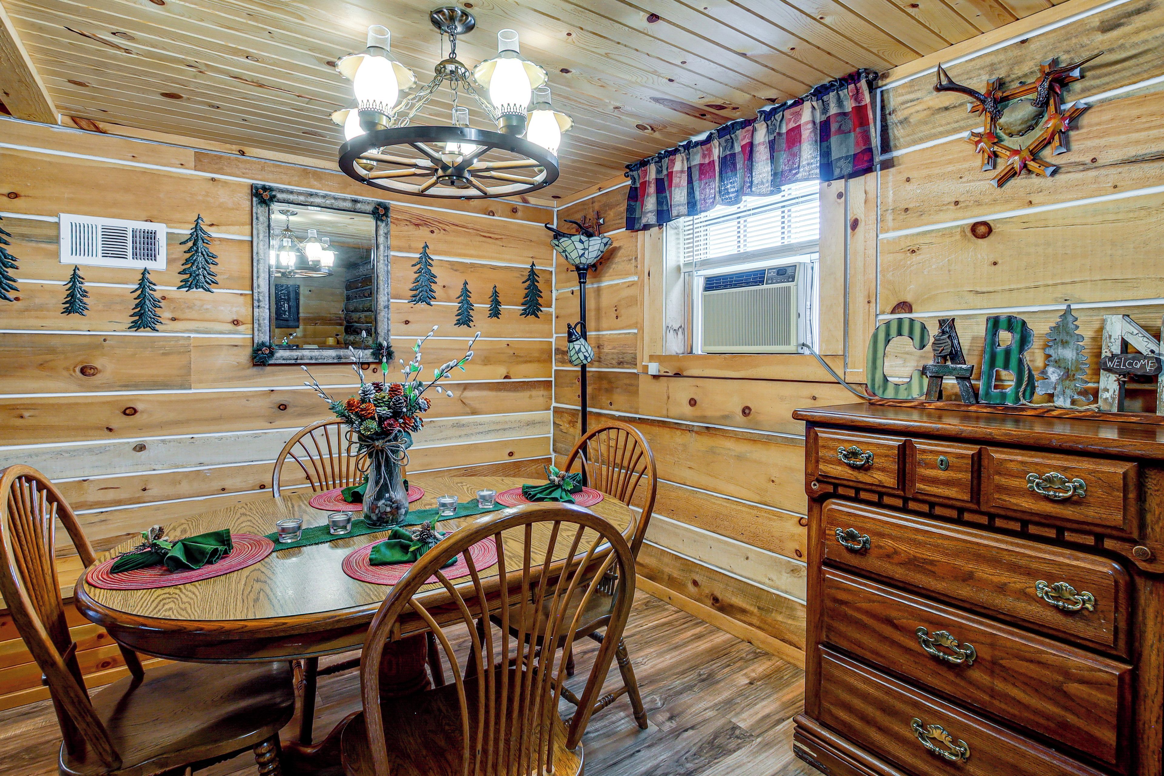 Ein Holzinterieur mit einem Esstisch, gedeckt für vier Personen, umgeben von Stühlen, einer Chandelüster und einer Kommode mit Schubladen.