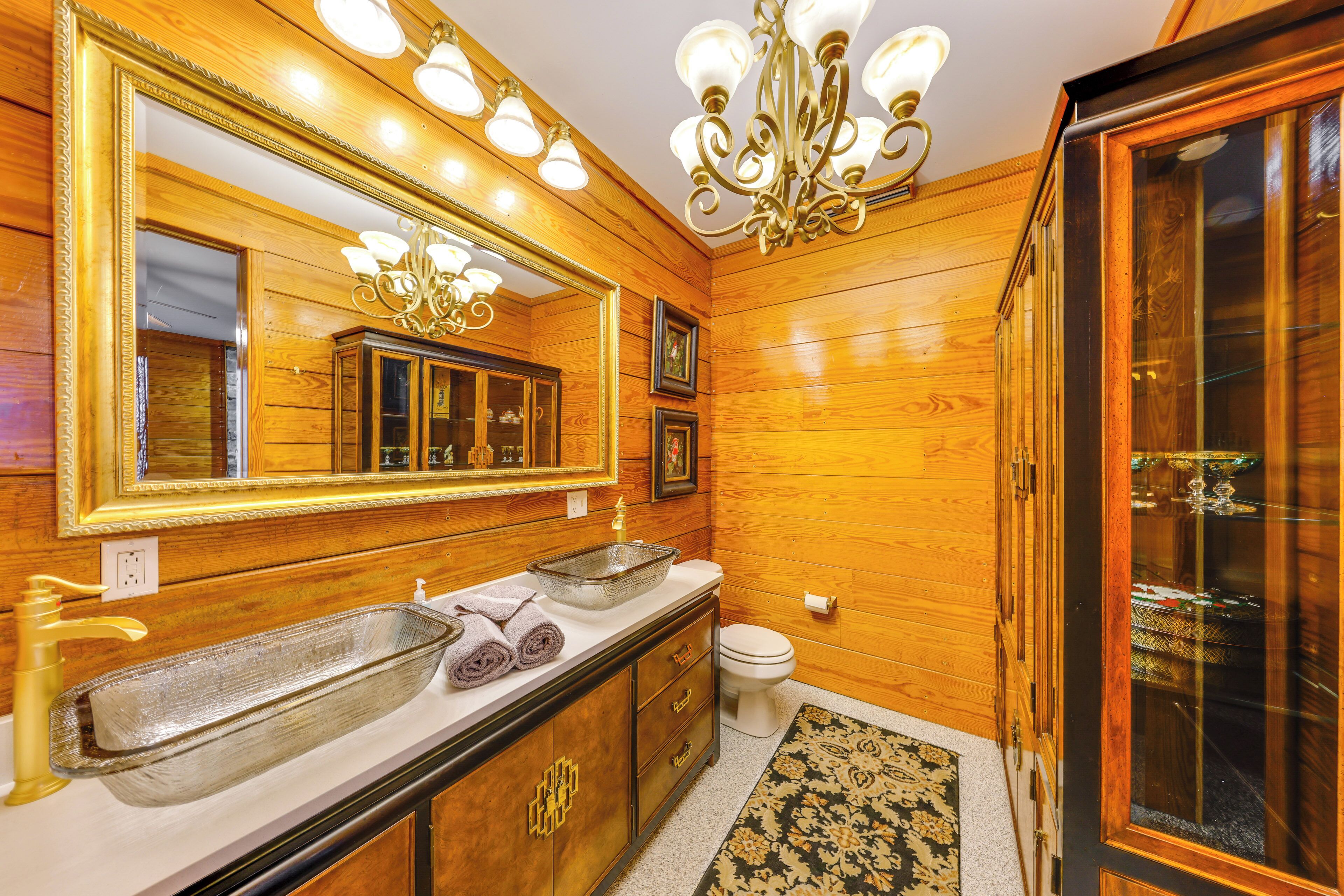 Un baño revestido de paneles de madera con un espejo grande, dos lavamanos, una araña y una ducha con paredes de vidrio.