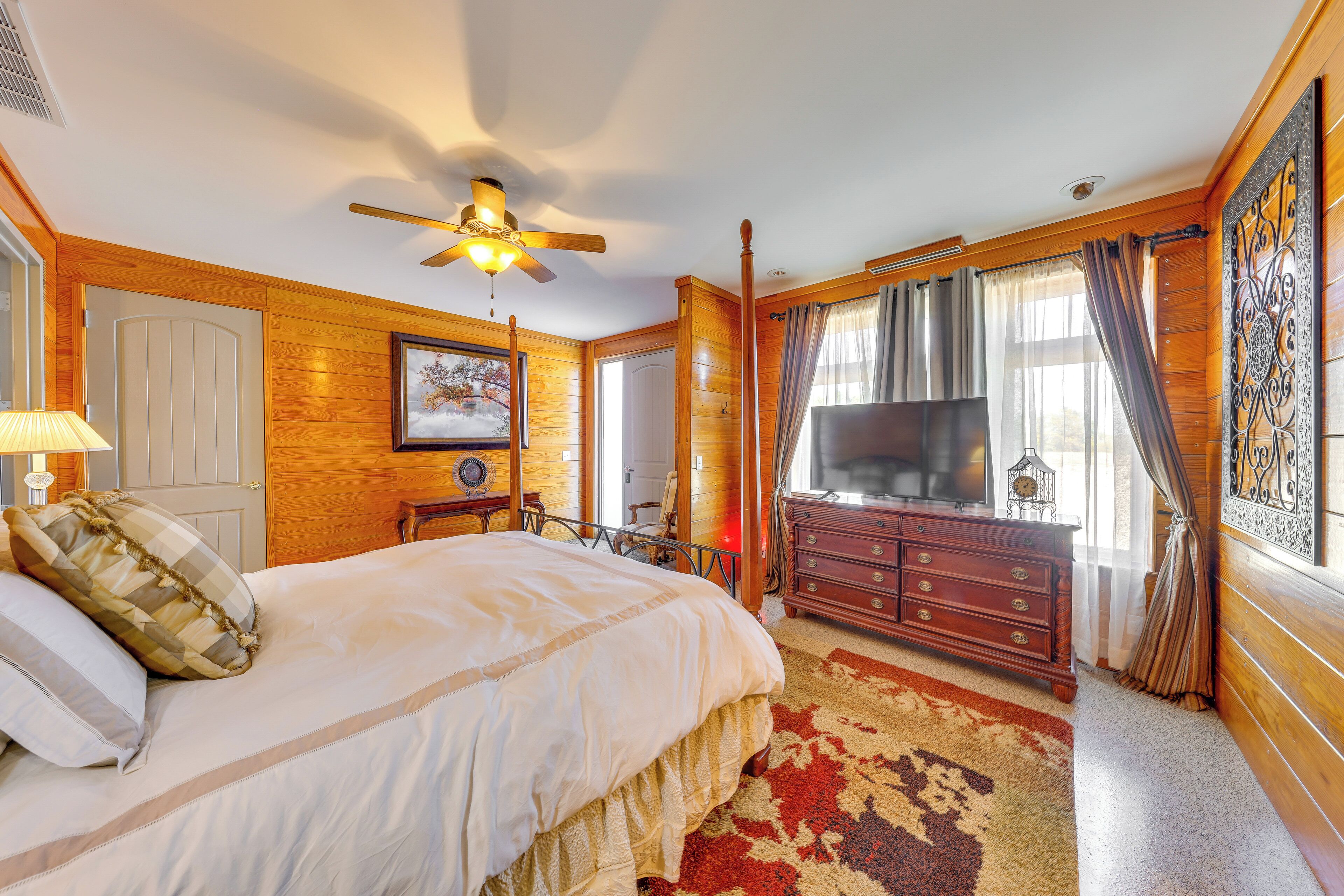 A bedroom with a large bed, wooden walls, a ceiling fan, a dresser, and a TV.