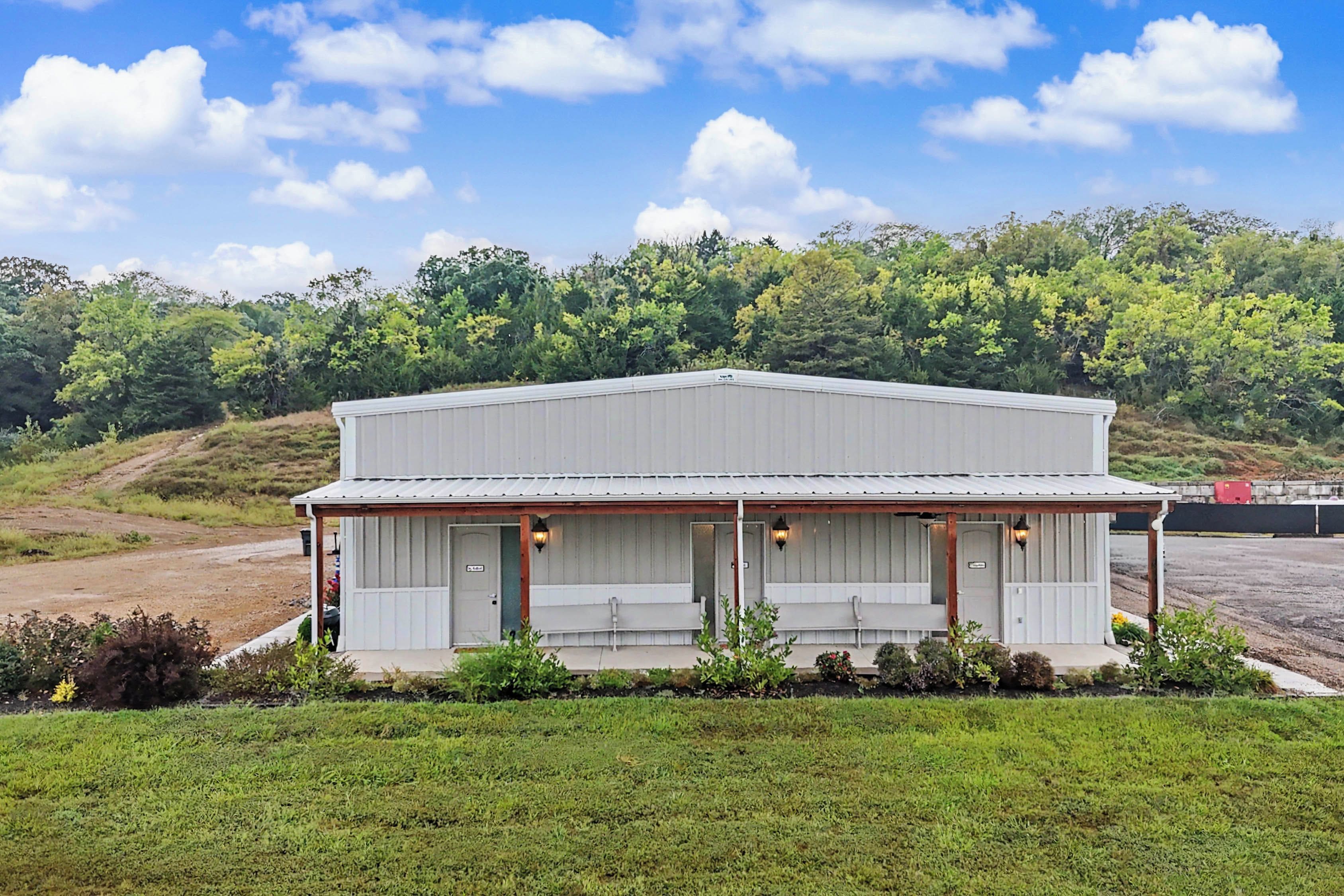 A single-story building with a flat roof, a covered porch with two benches, and a sign indicating a business or service.