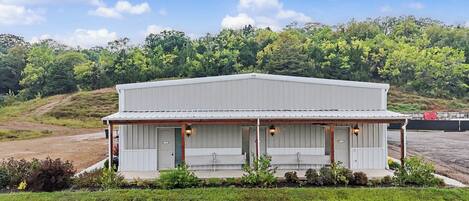 A single-story building with a flat roof, a covered porch with two benches, and a sign indicating a business or service.