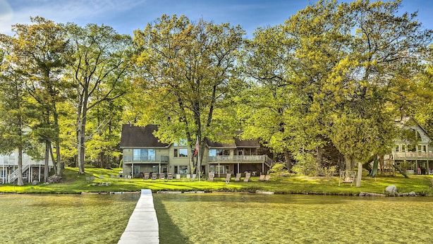 A lakeside property with a wooden dock leading to a house with multiple balconies and a deck.