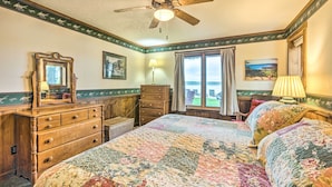 A bedroom with a large bed, a dresser, a ceiling fan, a window with curtains, and a view of the outdoors.