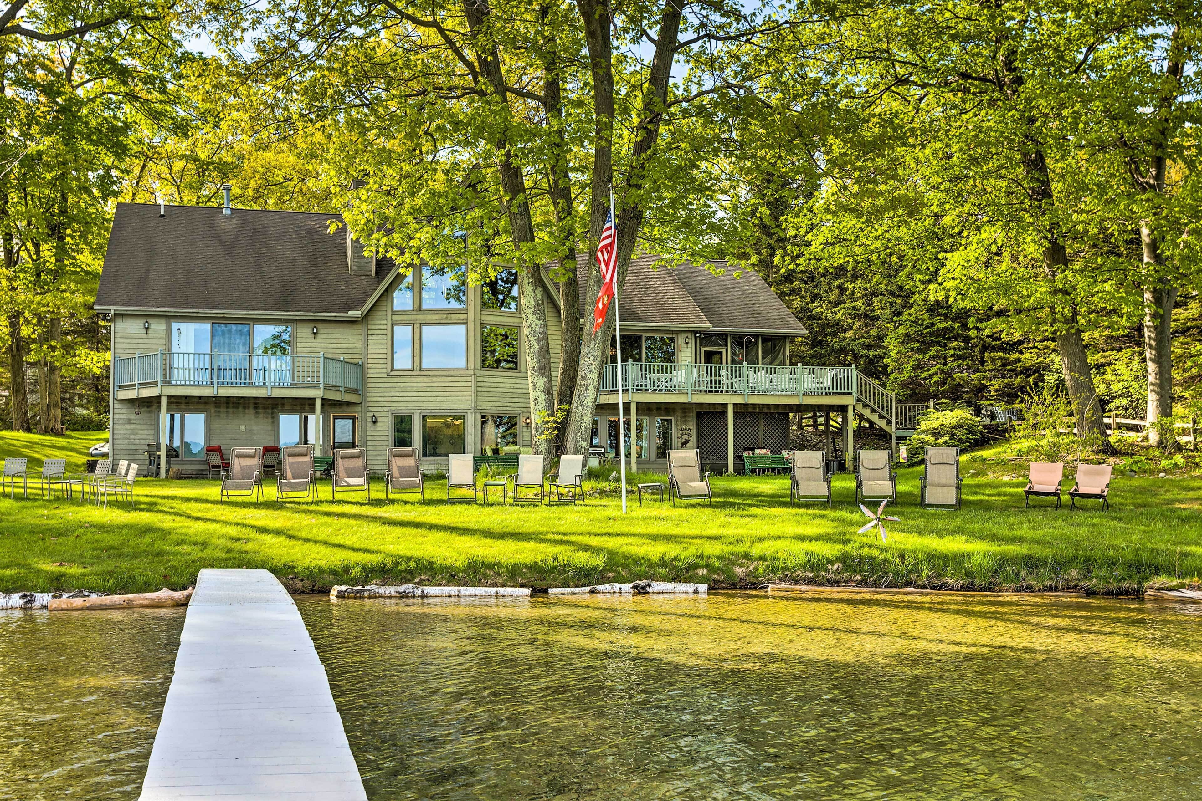 A two-story house with a balcony and a porch, surrounded by lush green trees and a small pond.
