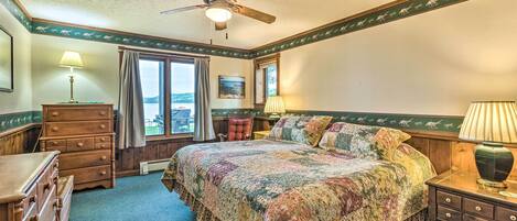 A bedroom with a large bed, a ceiling fan, a dresser, a nightstand, and a window with a view.