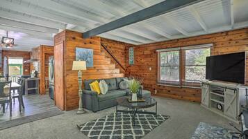 A cozy cabin interior with a dining area, a living room with a sofa and coffee table, and a TV on a wooden cabinet.