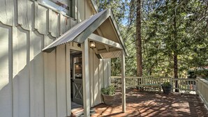 A wooden deck with a covered porch, potted plants, and a view of a forest. - Half-mi to Shaver Lake: Cabin w/ Wraparound Deck (Shaver Lake)
