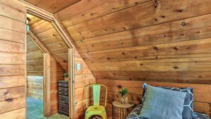 A wooden cabin bedroom with a lofted ceiling, a bed with patterned bedding, a green chair, a small round table with a plant, and a dresser with multiple drawers. - Half-mi to Shaver Lake: Cabin w/ Wraparound Deck (Shaver Lake)