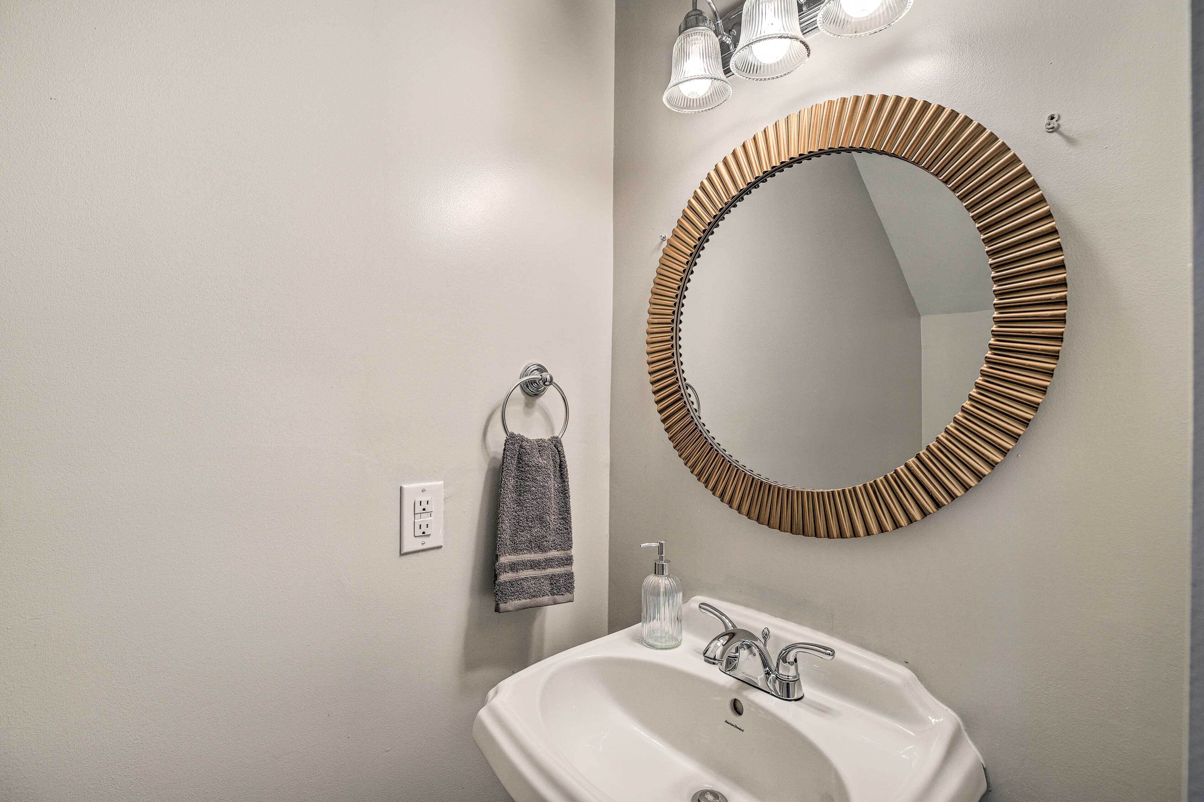 A bathroom with a white sink, a towel hanging on a ring, and a round mirror with a wooden frame.