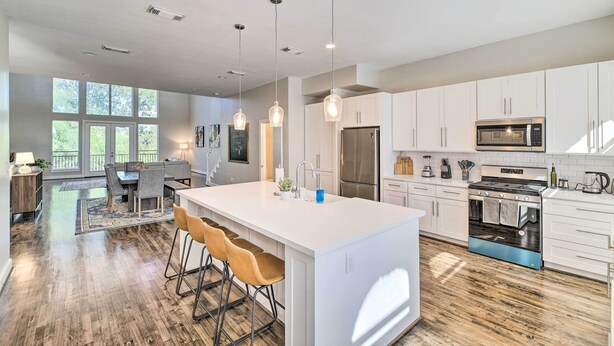 A modern kitchen with white cabinetry, a central island with bar stools, stainless steel appliances, and pendant lighting. - 3-story Houston Townhome: 1 Mi to Minute Maid Park (Houston)
