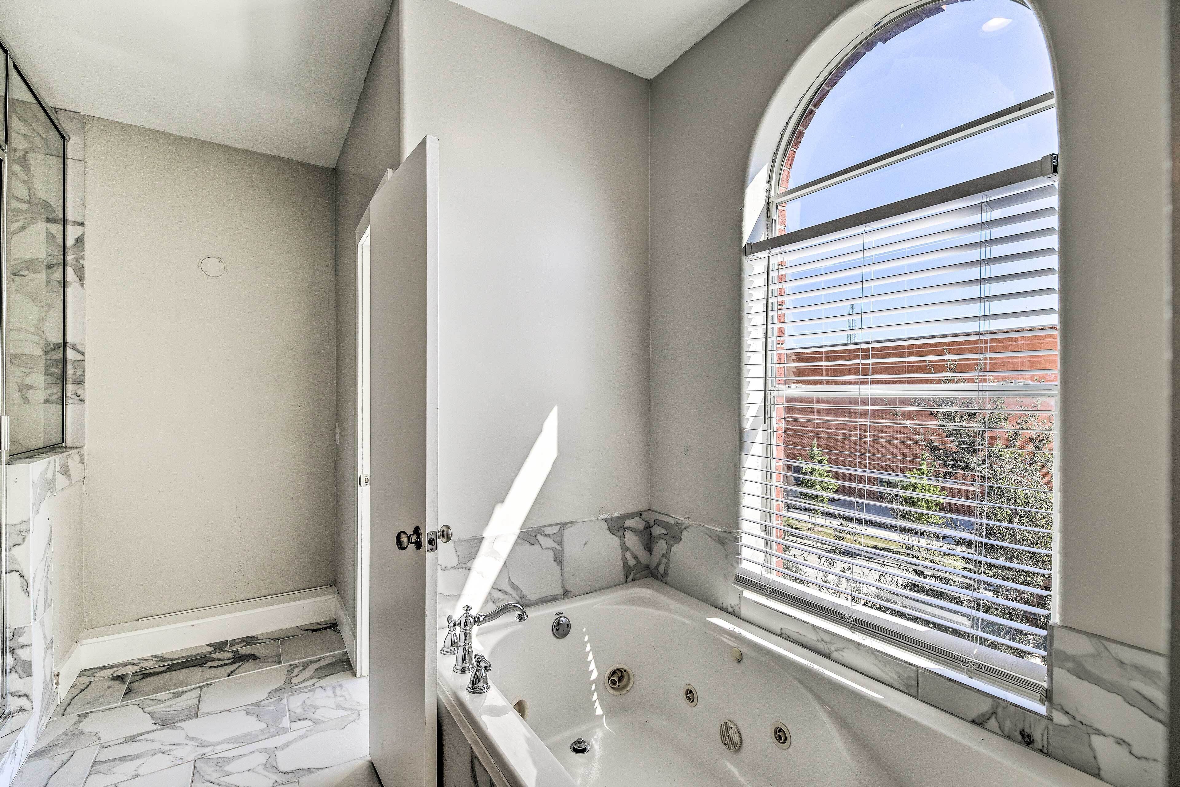 A bathroom with a marble floor, a bathtub, and a window with blinds.