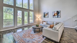 A spacious living room with large windows, a gray sofa, a round coffee table, and a patterned rug. - 3-story Houston Townhome: 1 Mi to Minute Maid Park (Houston)