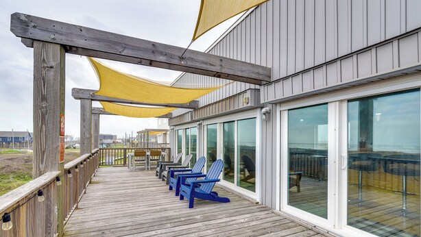 A wooden deck with blue chairs and yellow shade sails, overlooking a beach.