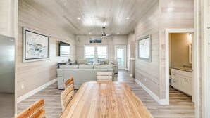 A spacious living area with a long wooden dining table, a sofa, and a kitchen area with white cabinets. - Seven Palms 3 Bedroom Home by RedAwning (Fulton)