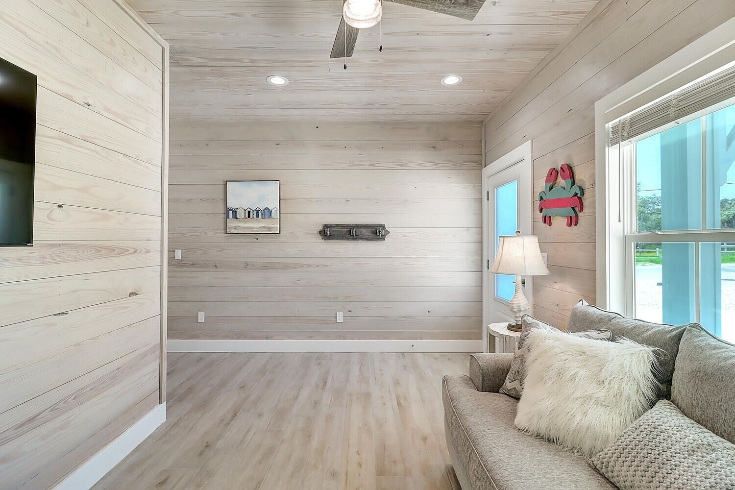 Une pièce spacieuse avec un lambris en bois, une grande fenêtre et un coin salon confortable agrémenté d’une lampe et de coussins.