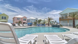 A swimming pool with white lounge chairs, a blue water feature, and colorful buildings in the background. - Seven Palms 3 Bedroom Home by RedAwning (Fulton)
