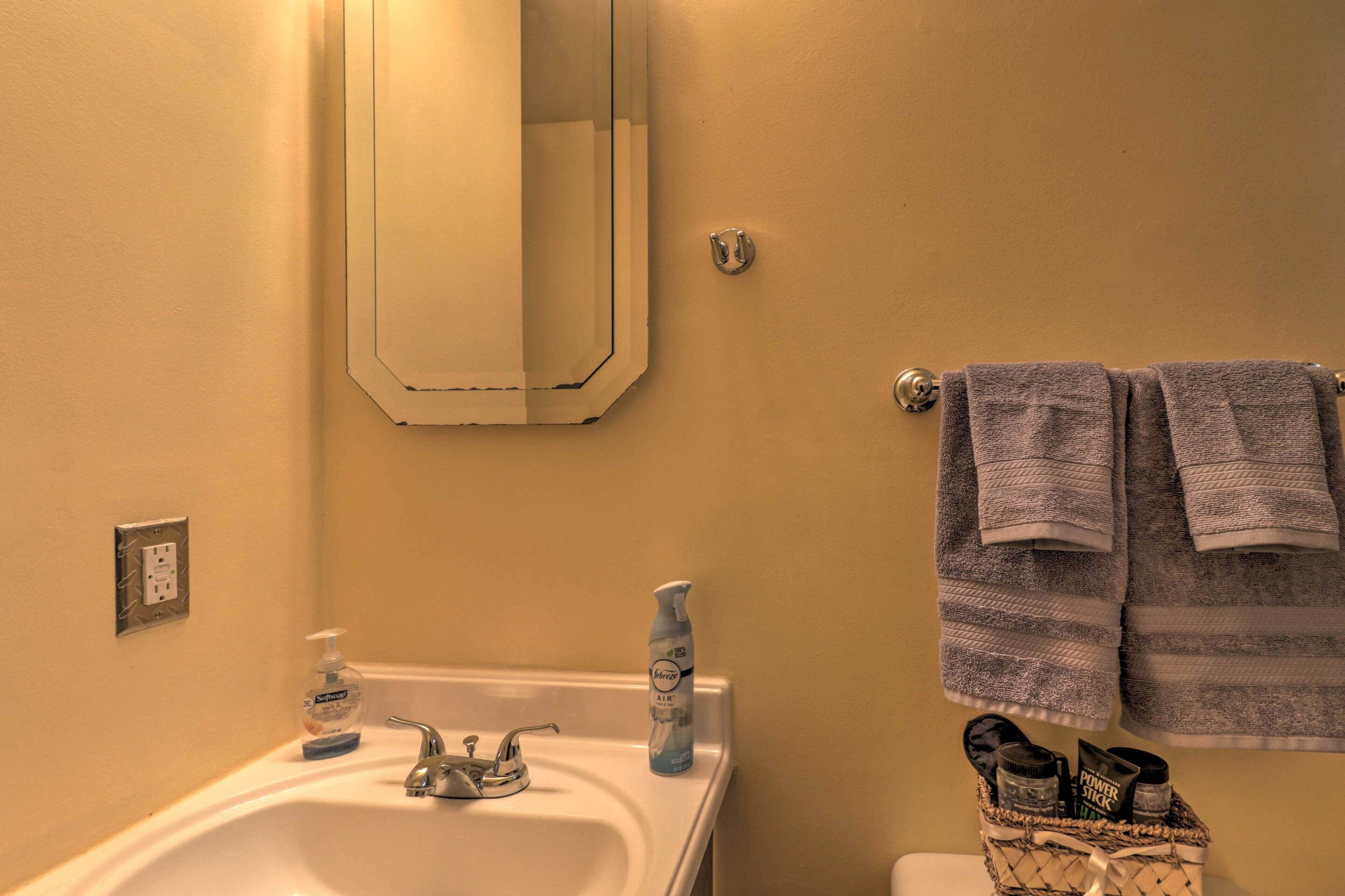 Une salle de bain équipée d’un lavabo, d’un miroir, d’un porte-serviettes et d’un panier contenant des chaussons.