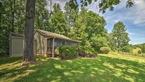 A single-story house with a porch, surrounded by a well-maintained lawn and tall trees. - Cozy Rixeyville Cottage w/ Deck, Grill, & Stabling (Rixeyville)