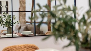 Un comedor con una mesa lista para dos, una silla tejida y un florero con plantas.