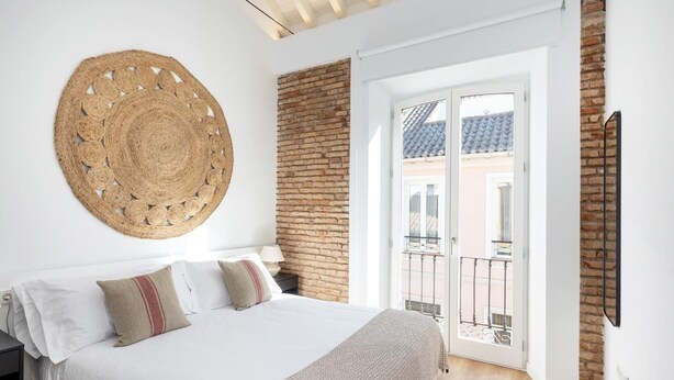 Un dormitorio con cama, un tapiz tejido en la pared, pared de ladrillo y puerta corrediza de vidrio hacia el exterior.