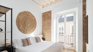 Un dormitorio con cama, un tapiz redondo tejido, pared de ladrillo y un balcón con barandilla.