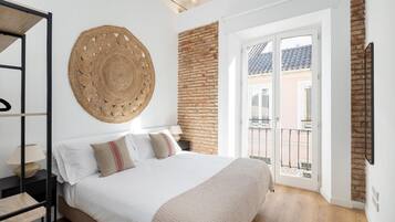 Un dormitorio con cama, un tapiz redondo tejido, pared de ladrillo y un balcón con barandilla.