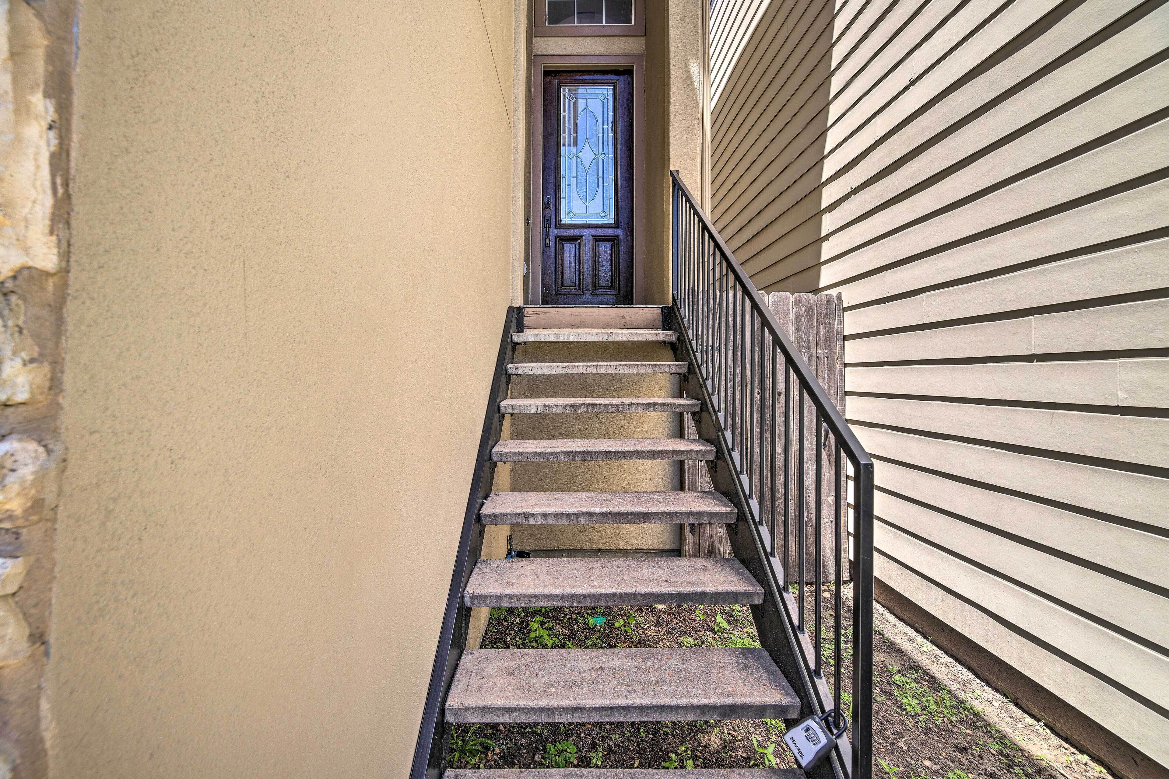 Una escalera estrecha que conduce a una puerta con un panel de vidrio decorativo, flanqueada por paredes de revestimiento color beige y una barandilla de metal.