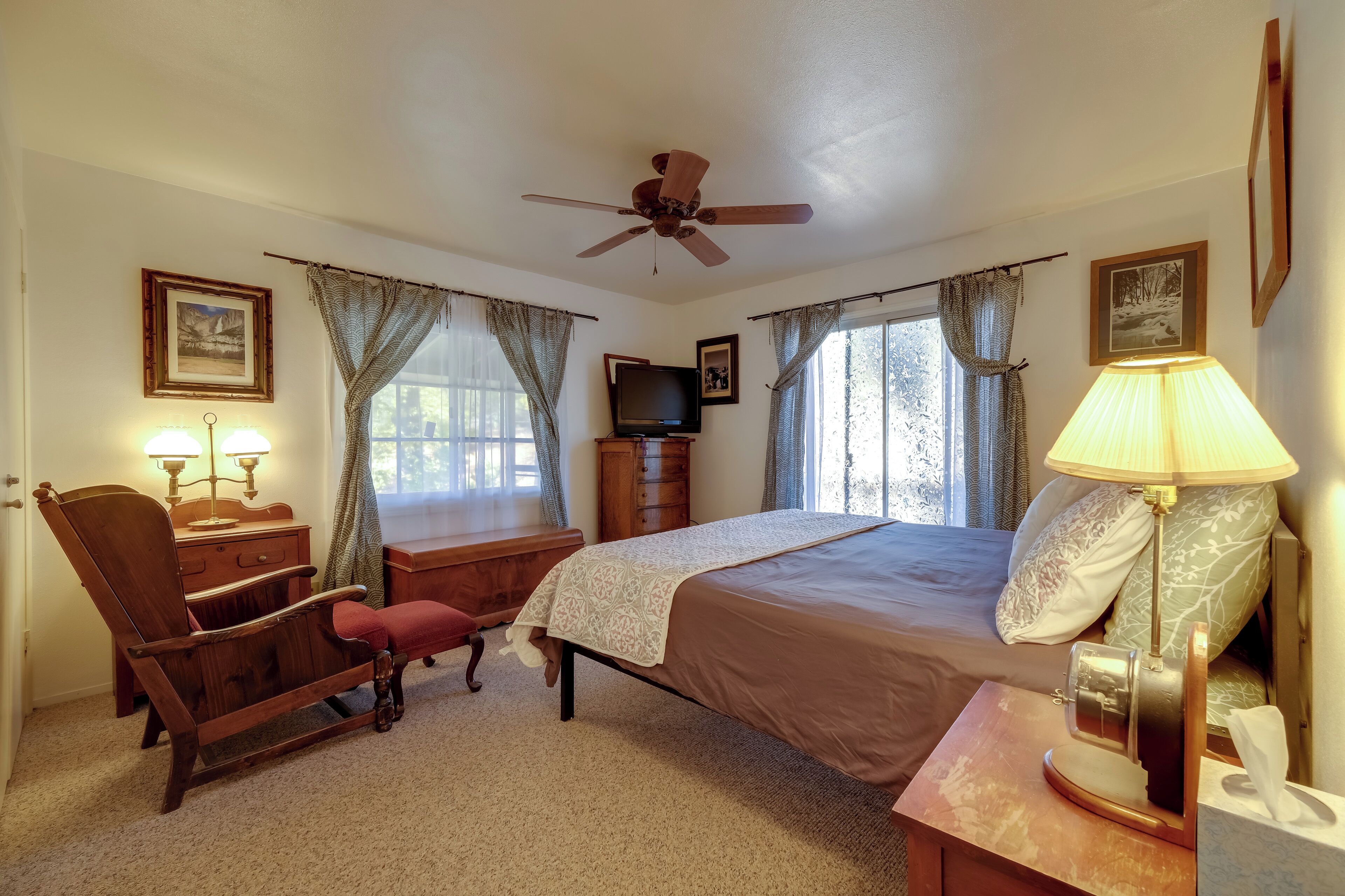 Ein Schlafzimmer mit Bett, Stuhl, Schreibtisch, Fernseher und Deckenventilator.