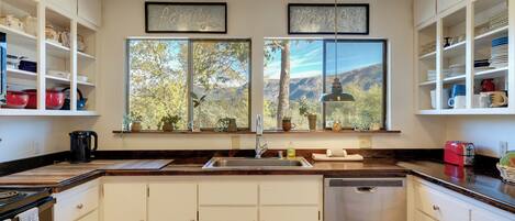 A kitchen with a large window, wooden cabinets, a sink, and a dishwasher.