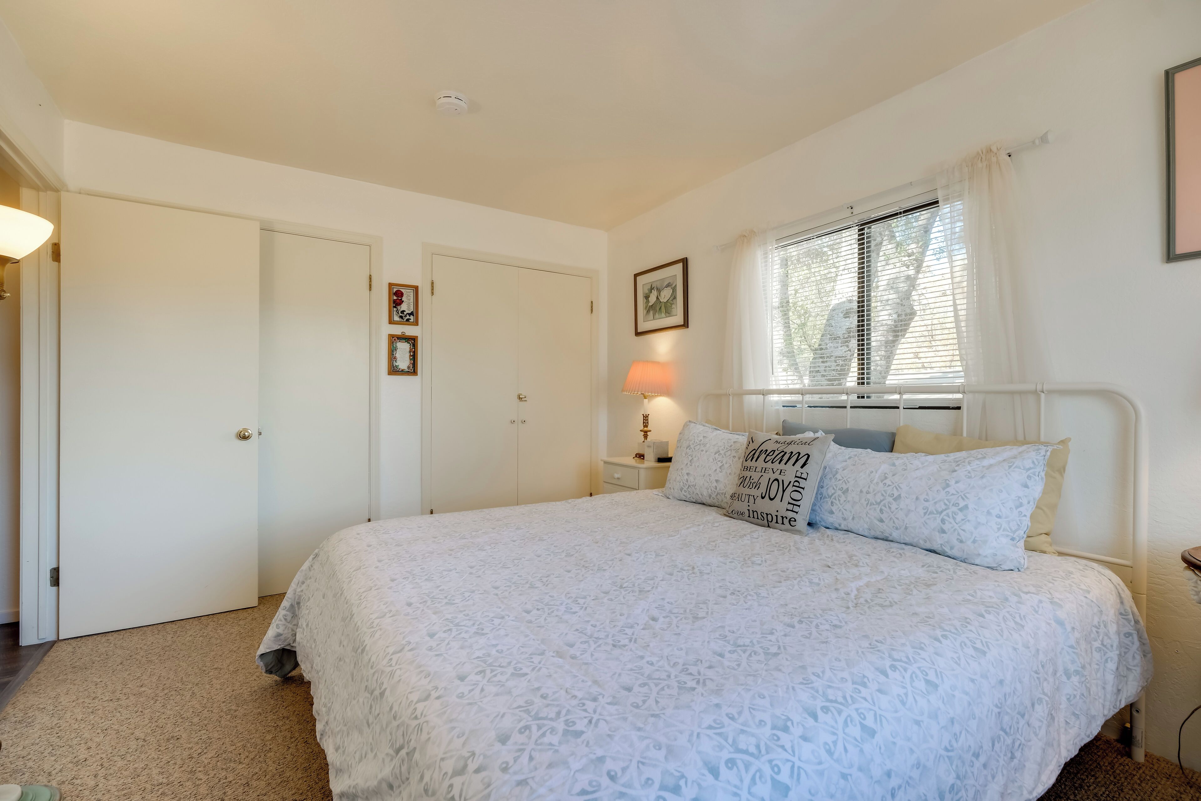 Een slaapkamer met een bed, een raam met gordijnen, een bedlamp en een deur.
