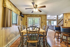 A dining area with a wooden table and chairs, a ceiling fan, and a view of the outdoors through large windows. - Cozy Bear Den Cabin Game Room & Golf Cart (Pocono Lake)