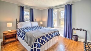 Ein Schlafzimmer mit Bett, Nachttisch, Lampe, Fenster mit Vorhängen und einem Rollstuhl.
