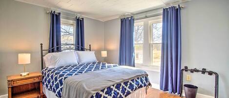 A bedroom with a bed, nightstand, lamp, window with curtains, and a wheelchair.