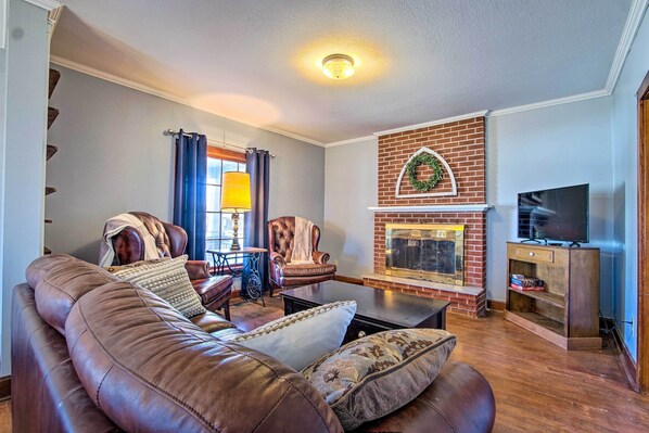 A living room with a leather sofa, a fireplace, a television, and a brick wall.