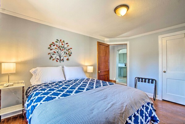 A bedroom with a bed, two bedside tables, a nightstand, a wall-mounted artwork, and a door leading to another room. - Quiet Family Home - 12 Miles to Pomona State Park! (Osage City)