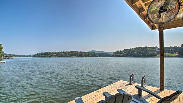 A wooden deck with two Adirondack chairs and a ceiling fan, overlooking a calm lake with a forested island in the distance. - Kayaks, Dock: Waterfront Escape on Lake Hamilton! (Hot Springs)