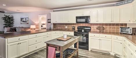 A modern kitchen with white cabinets, a central island, a microwave, a stove, and a toaster.