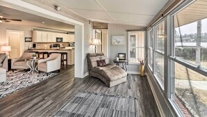 A spacious living area with a sofa, chairs, and a dining table. There is a kitchen in the background with cabinets and appliances. The room has large windows and a view of the outdoors. - Kayaks, Dock: Waterfront Escape on Lake Hamilton! (Hot Springs)