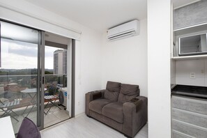 A modern apartment with a sliding glass door leading to a balcony, a grey sofa, and a built-in kitchen unit. - Vossa Bossa Vila Madalena Diseño (São Paulo)