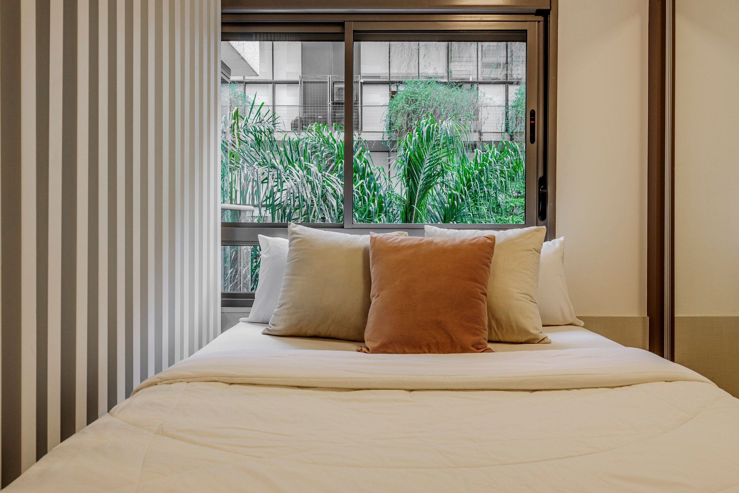 Une chambre d’hôtel avec un lit, une fenêtre donnant sur un paysage verdoyant et des rideaux à rayures.