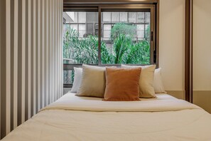 Una habitación de hotel con cama, ventana y vistas a la vegetación, además de cortinas a rayas.