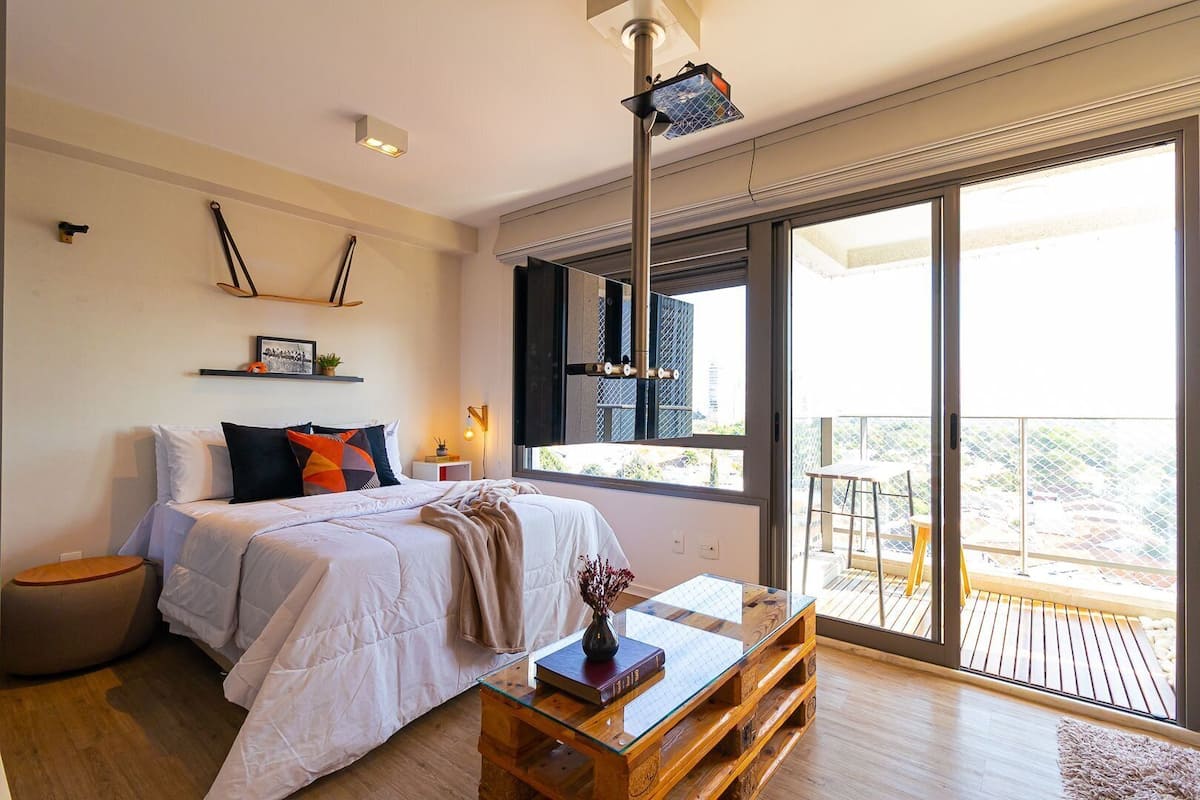 A modern bedroom with a large bed, a glass coffee table, and a balcony with a view.