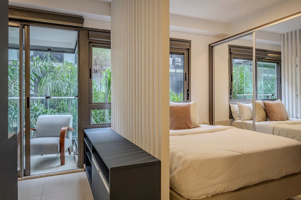 A modern bedroom with a large sliding glass door leading to a balcony, a sofa, and two beds with pillows.