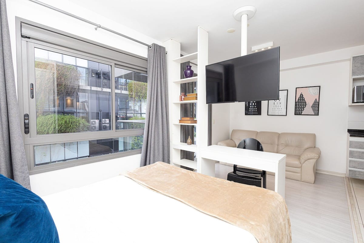 A modern bedroom with a large bed, a TV mounted on the wall, a sofa, and a window with curtains.